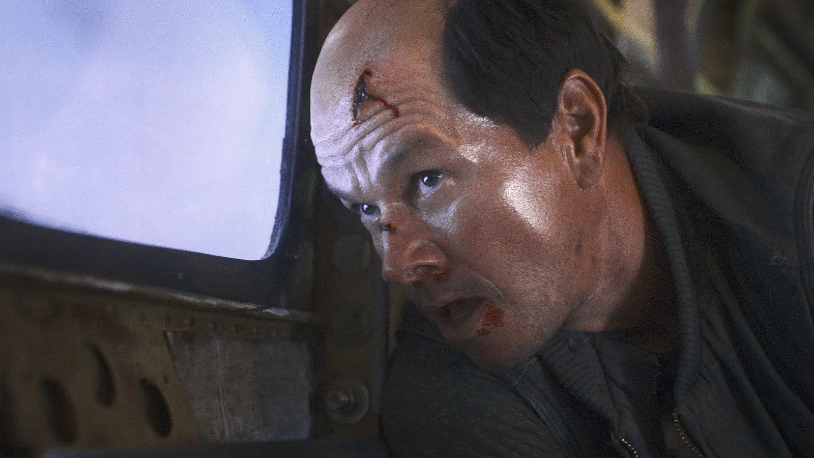 Mark Wahlberg mit Verletzungen im Gesicht und Halbglatze, blickt aus dem Flugzeugfenster