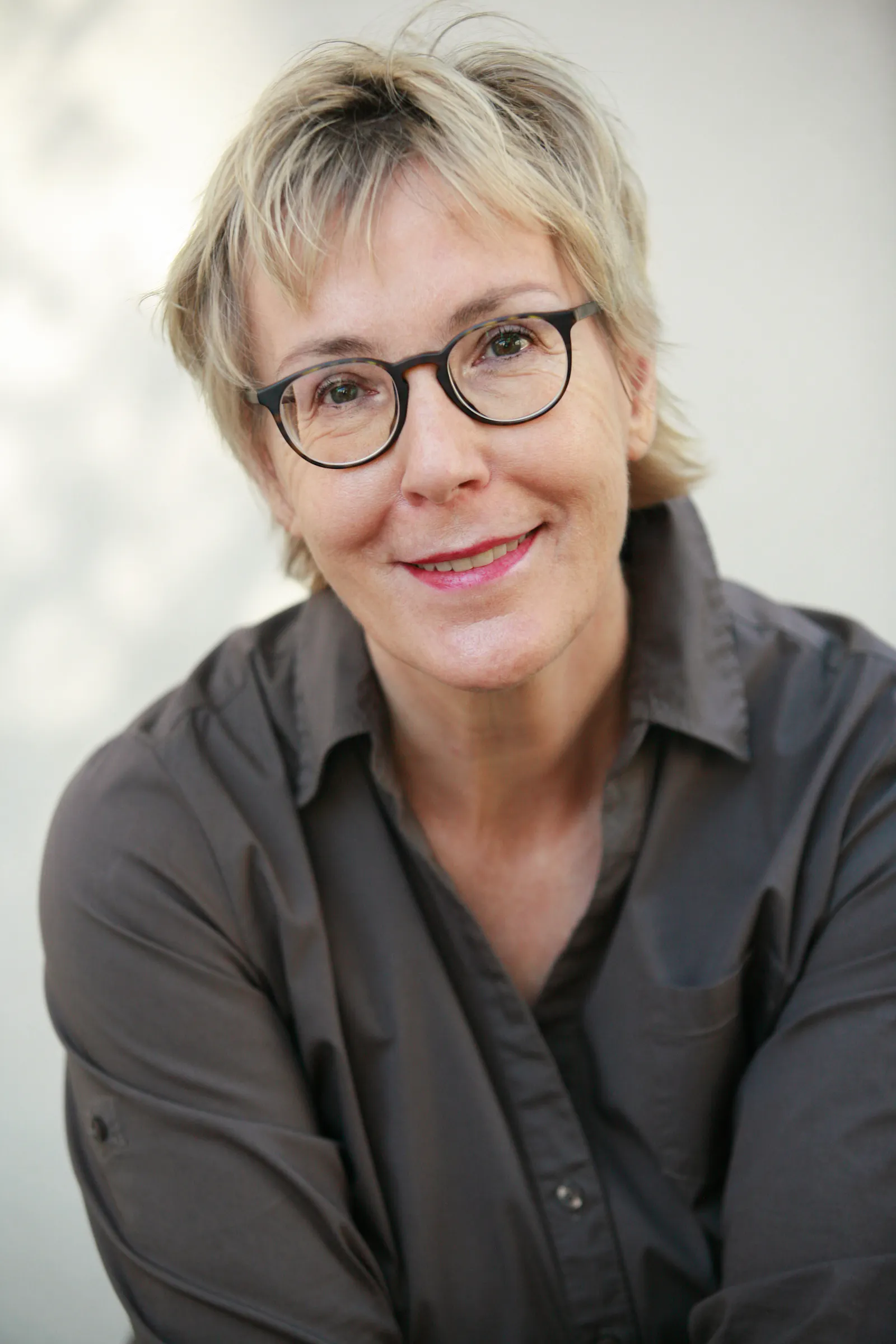 Eine Frau mit dunkler Brille und hellen, kurze Haaren schaut freundlich in die Kamera.