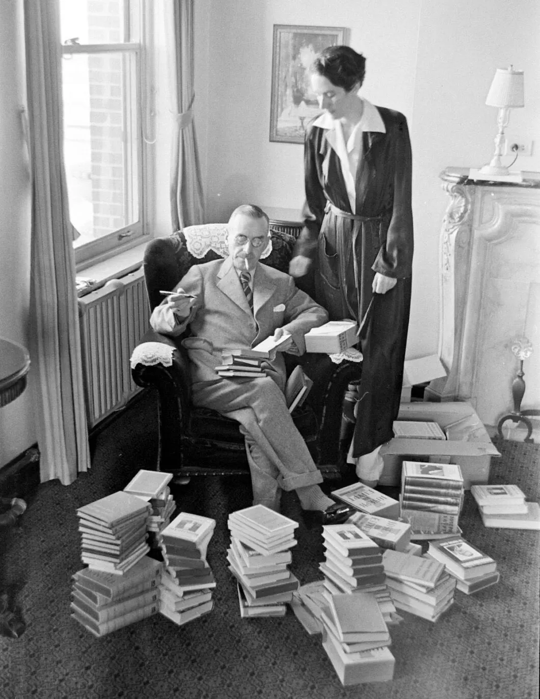 Thomas Mann sitzt umringt von seinen Büchern, hinter ihm steht seine Frau Katia Mann.