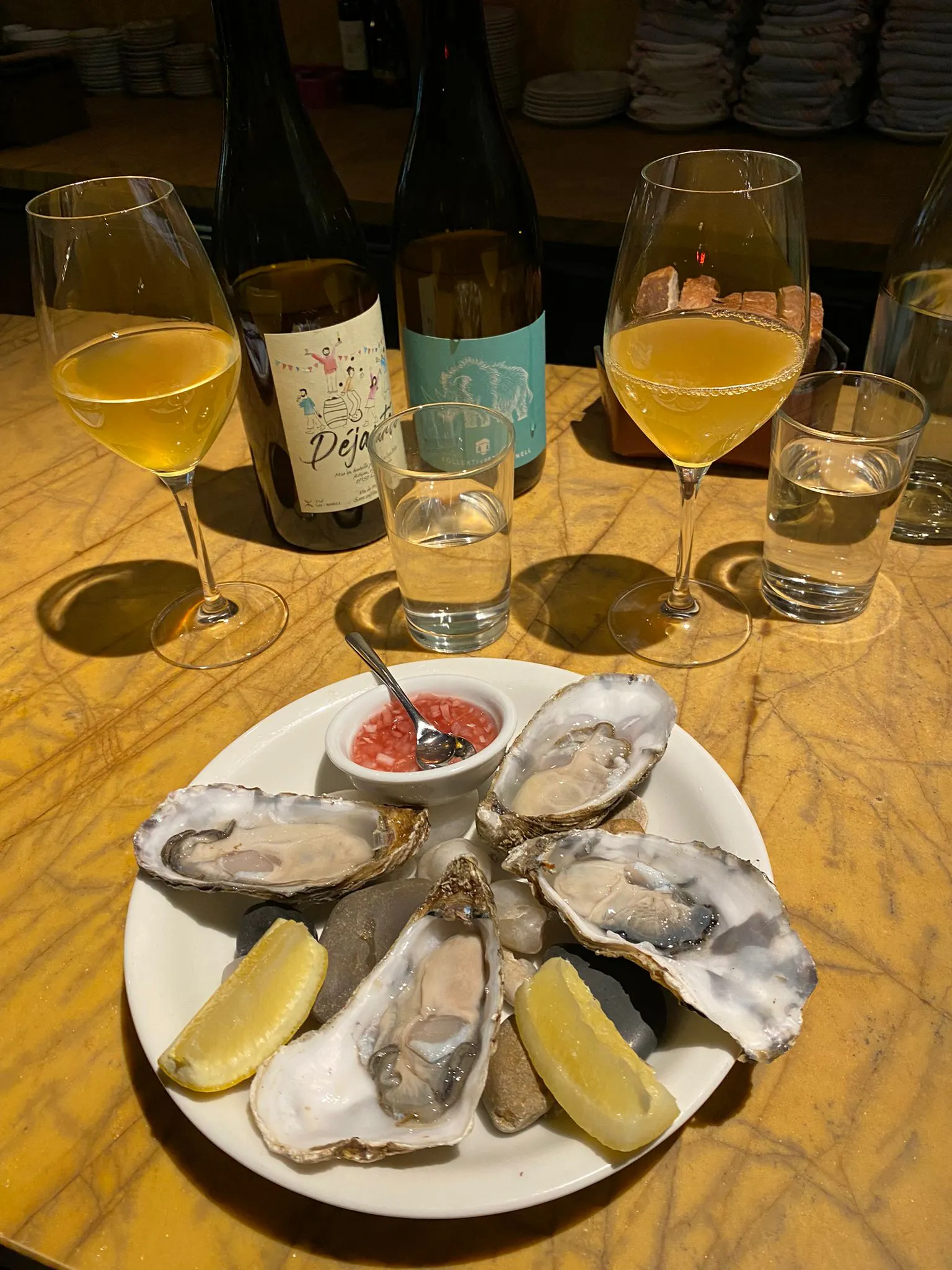 Frische Austern auf einem Teller und zwei Weinflaschen und zwei Weingläser im Hintergrund