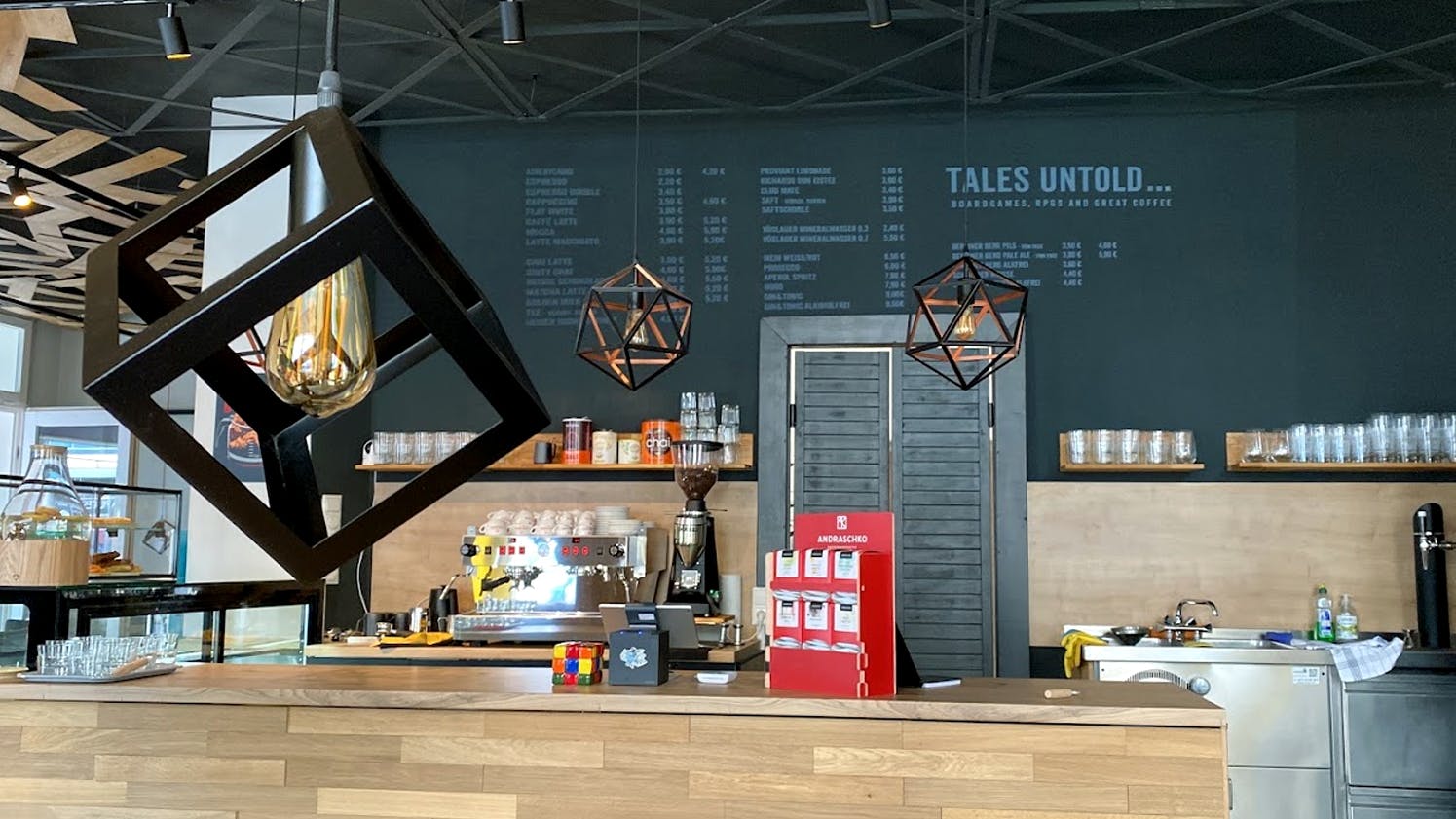 Der Tresen von Tales Untold in warmen Holztönen. Im Hintergrund ist die Getränkekarte auf eine Wandtafel geschrieben.