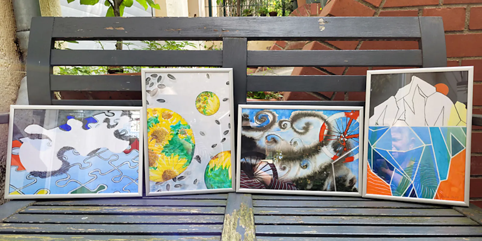 Schnappschuss von 4 Aquarellen auf einer Gartenbank mitden Titeln:  Freiheit, Sonnenblumen, Rückenwind sowie Bergen und Fasssauna.