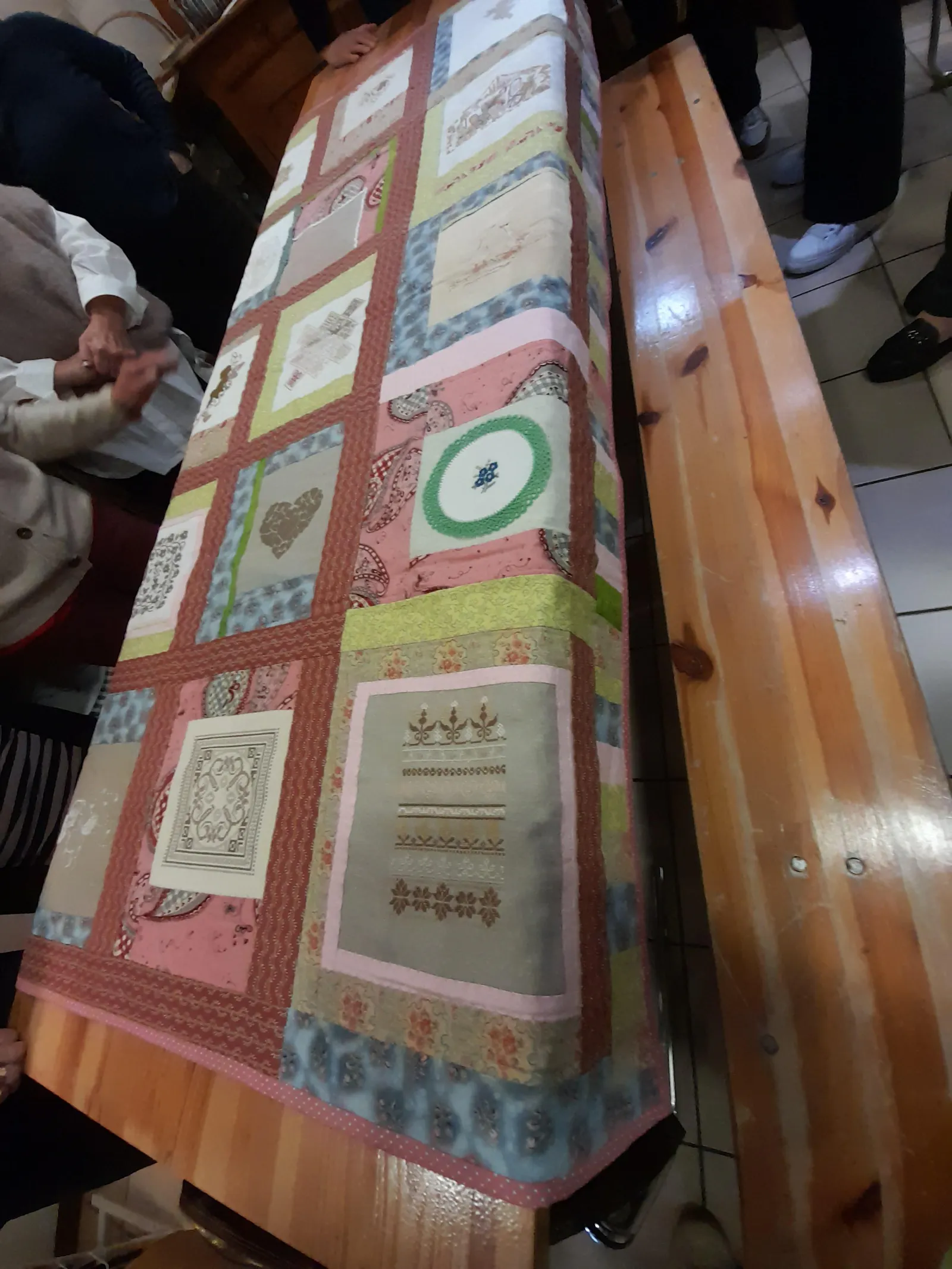 A long beer table for showing the finished blanket, the crafters standing around: feet and arms visible.