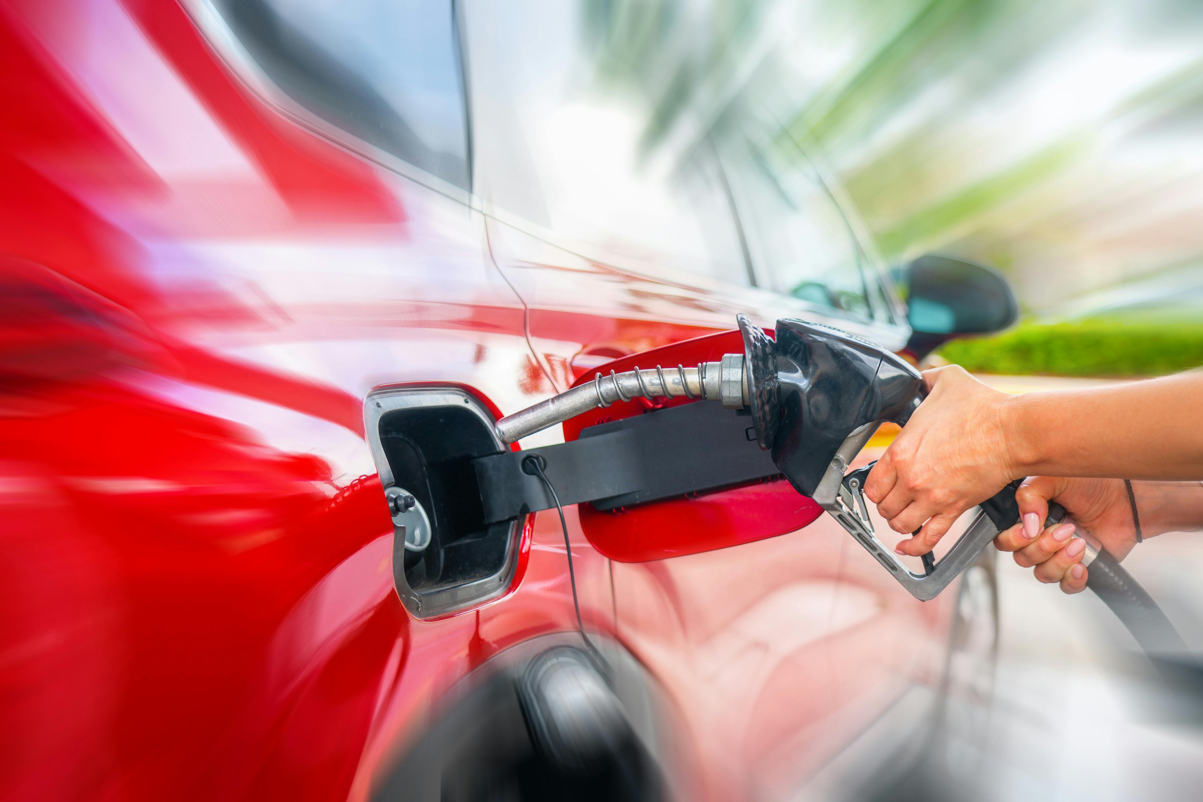 Auf dem Bild ist eine Hand zu sehen, die eine Zapfpistole in den Tank eines roten Autos hält.