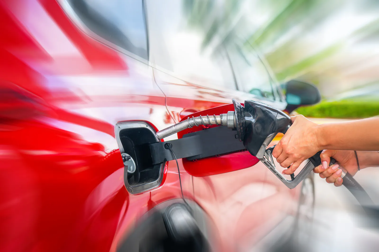 Auf dem Bild ist eine Hand zu sehen, die eine Zapfpistole in den Tank eines roten Autos hält.