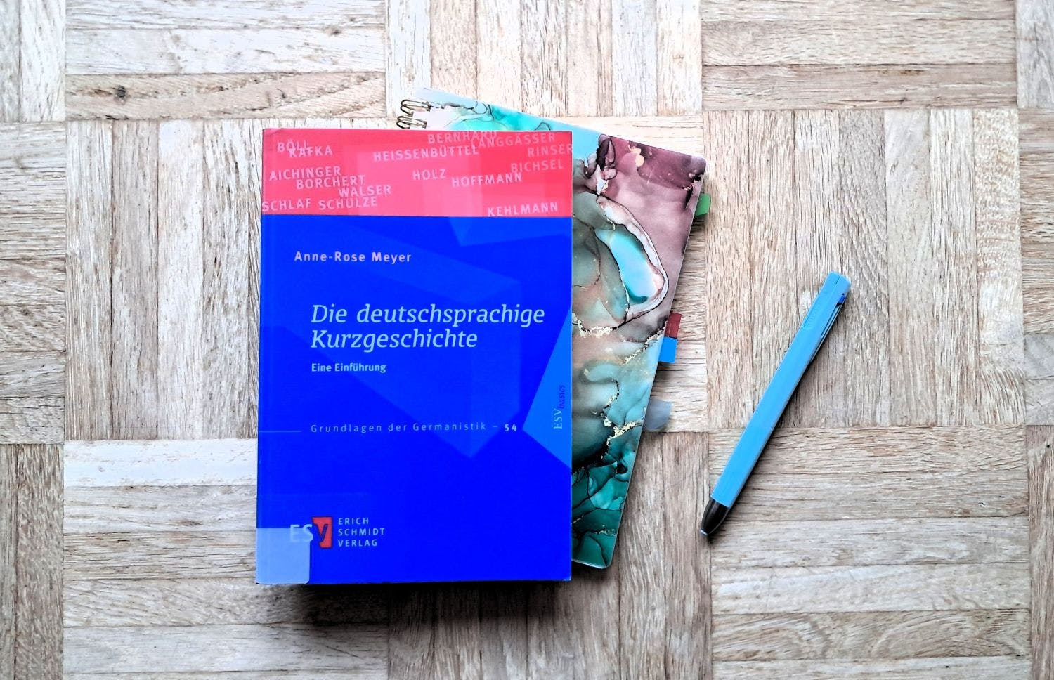 Buch "Die deutschsprachige Kurzgeschichte" liegt auf einem Notizbuch, daneben ein blauer Kugelschreiber.