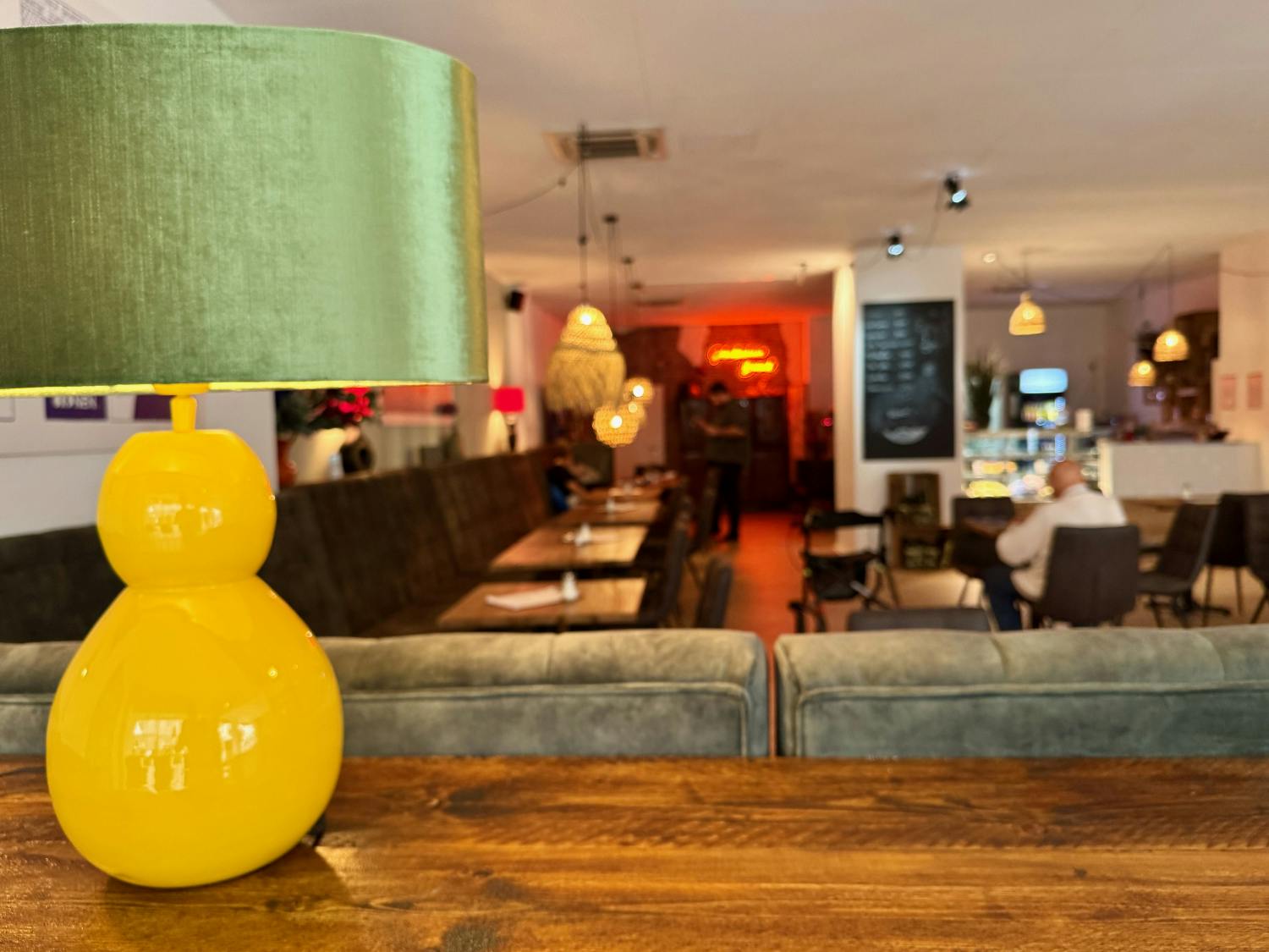 Eine gelb-grüne Stehlampe auf einem Tisch mit unscharfem Blick in das Café im Hintergrund