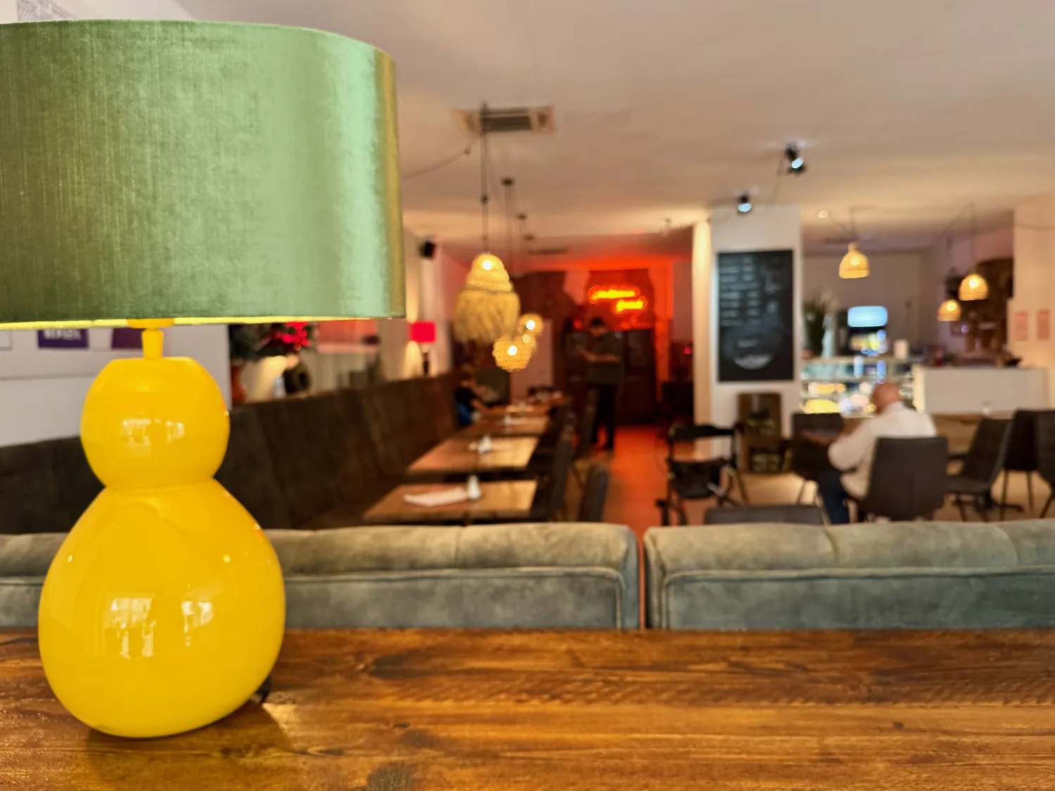 Eine gelb-grüne Stehlampe auf einem Tisch mit unscharfem Blick in das Café im Hintergrund
