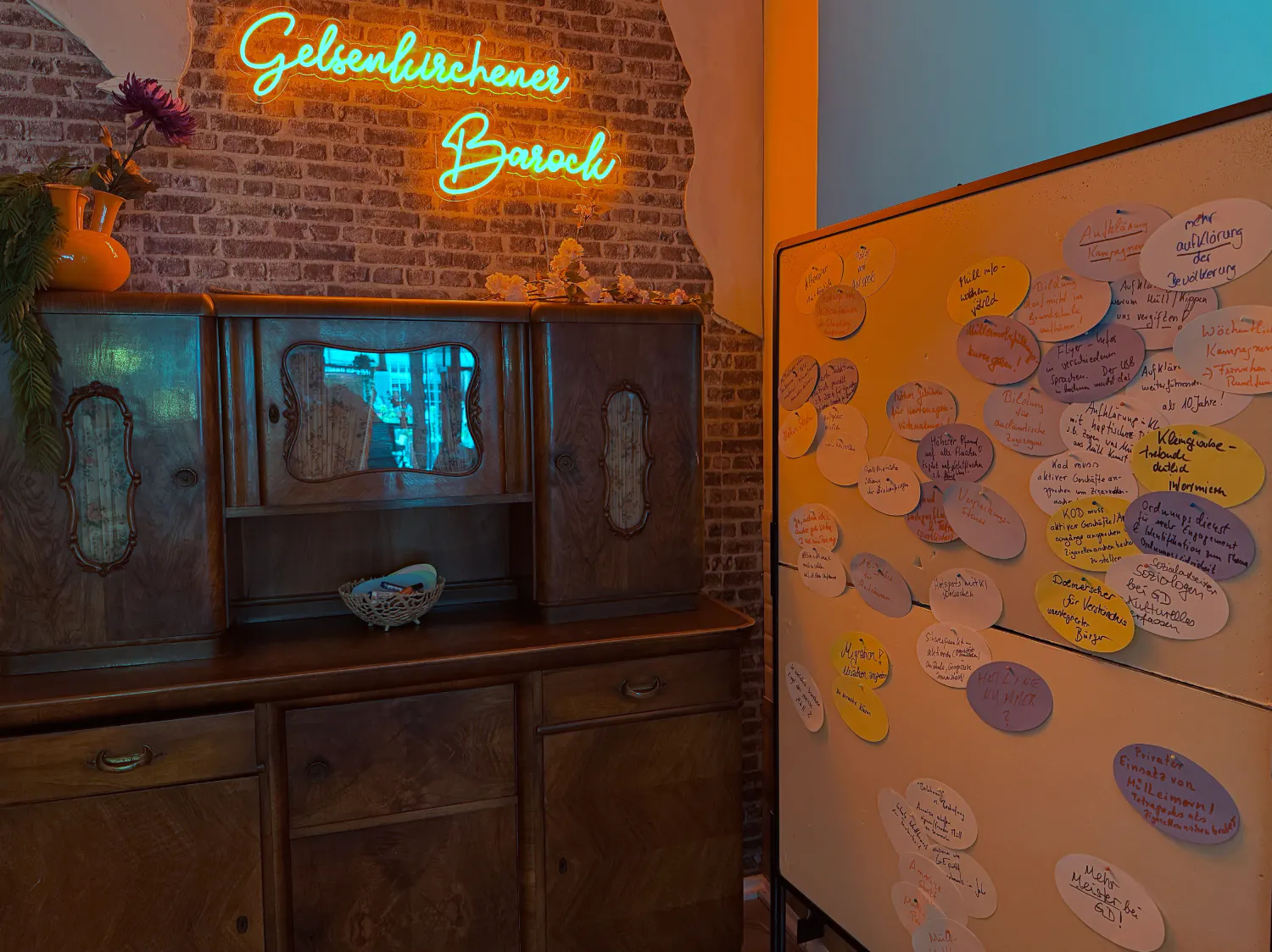 Eine Leuchtschrift über einem Küchenschrank und einer Pinnwand zeigt den Begriff „Gelsenkirchner Barock“