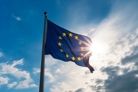 Eine EU-Flagge flattert im Wind, im Hintergrund sieht man den blauen Himmel mit ein paar weißen Wolken.