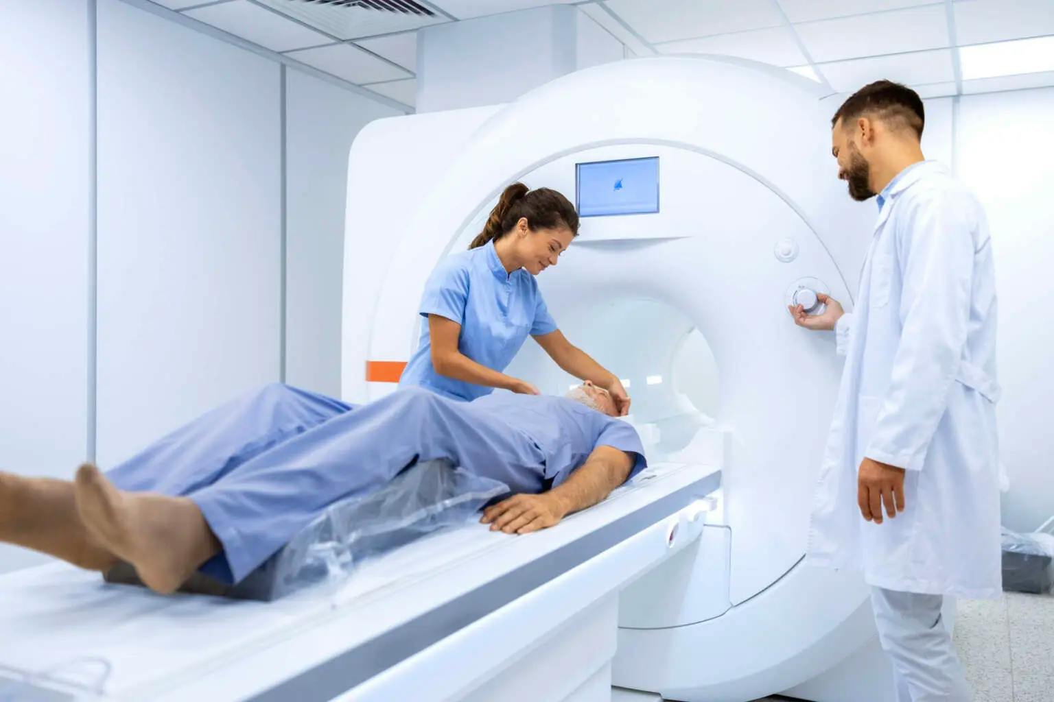 Ein Patient wird in einen Computer-Tomographen geschoben. Eine Pflegefachfrau und ein Arzt überwachen die Untersuchung