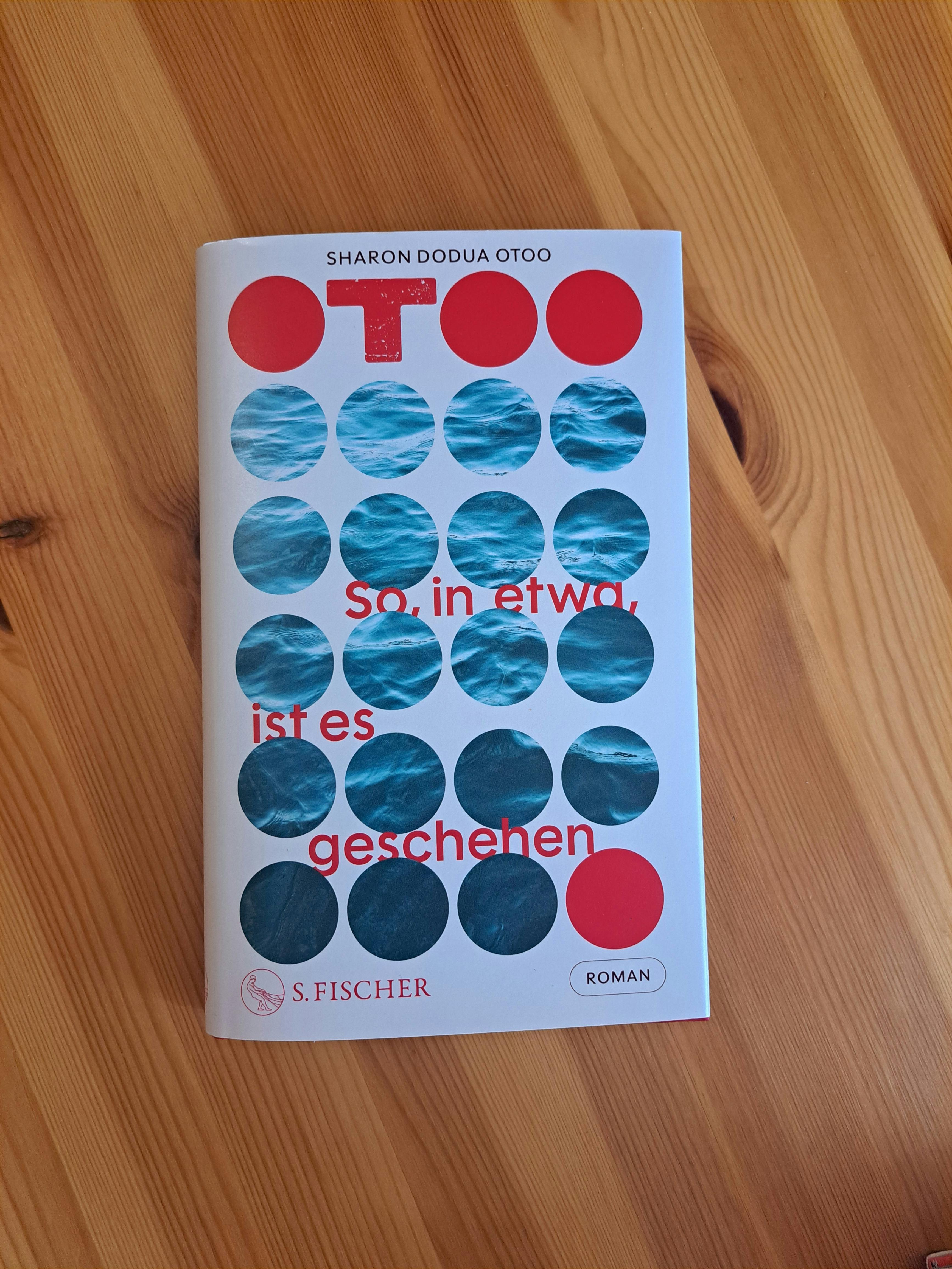 Eine Kopie des Buches "So, in etwa, ist es geschehen" von Sharon Dodua Otoo liegt auf einem Holzboden.