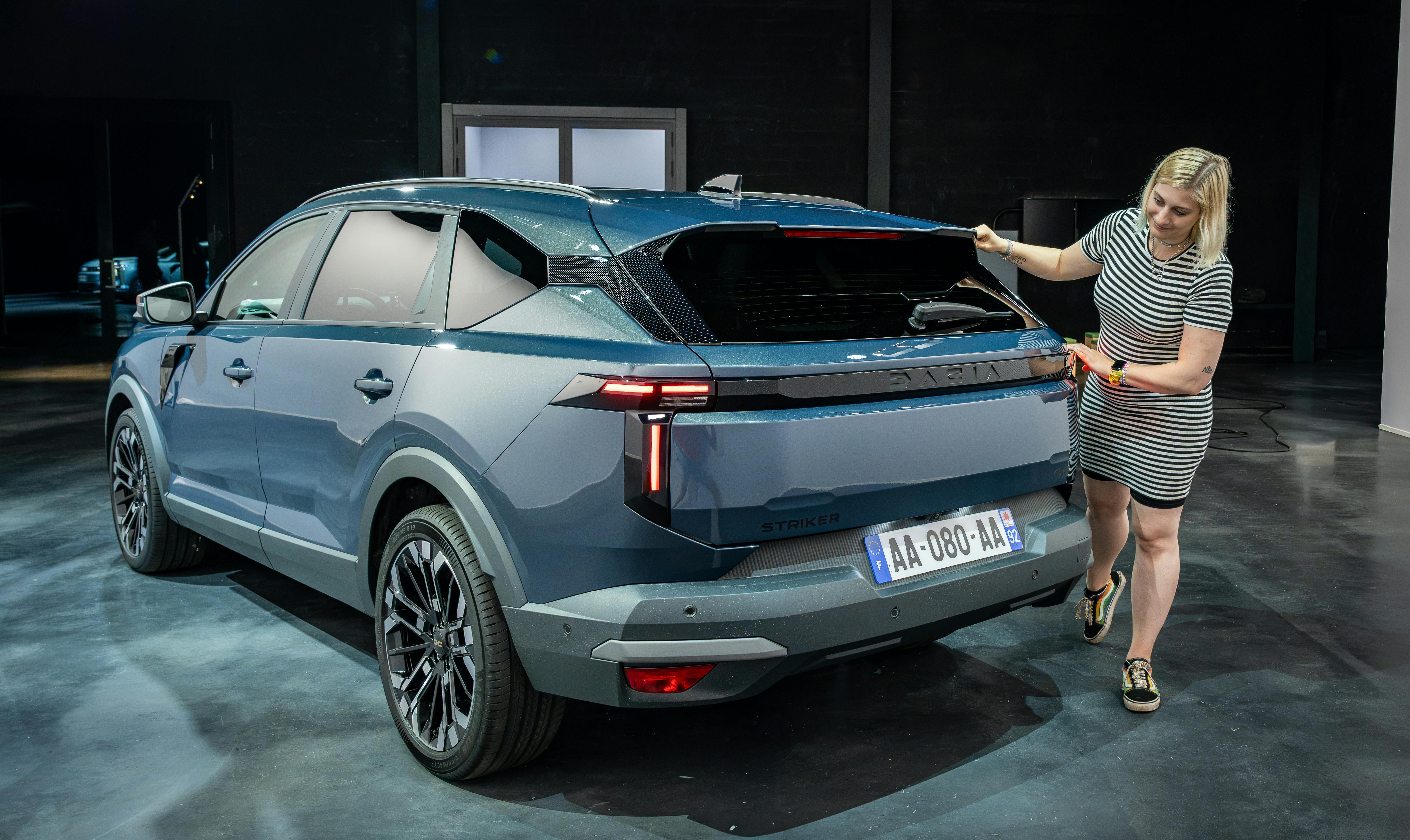 Rückseite des hellblauen Dacia Striker, rechts daneben zeigt Carconny auf die Rückseite