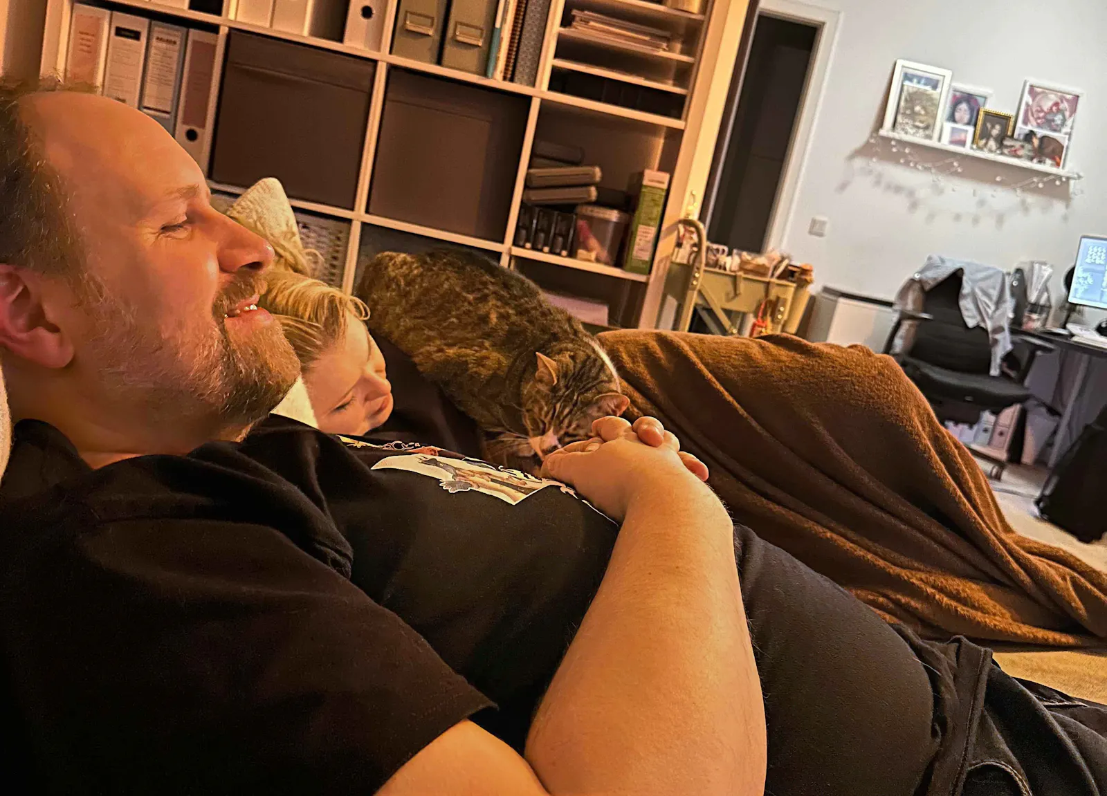 Alex und Rieke liegen nebeneinander auf dem Sofa. Auf Rieke liegt ihr dicker Kater Salem.