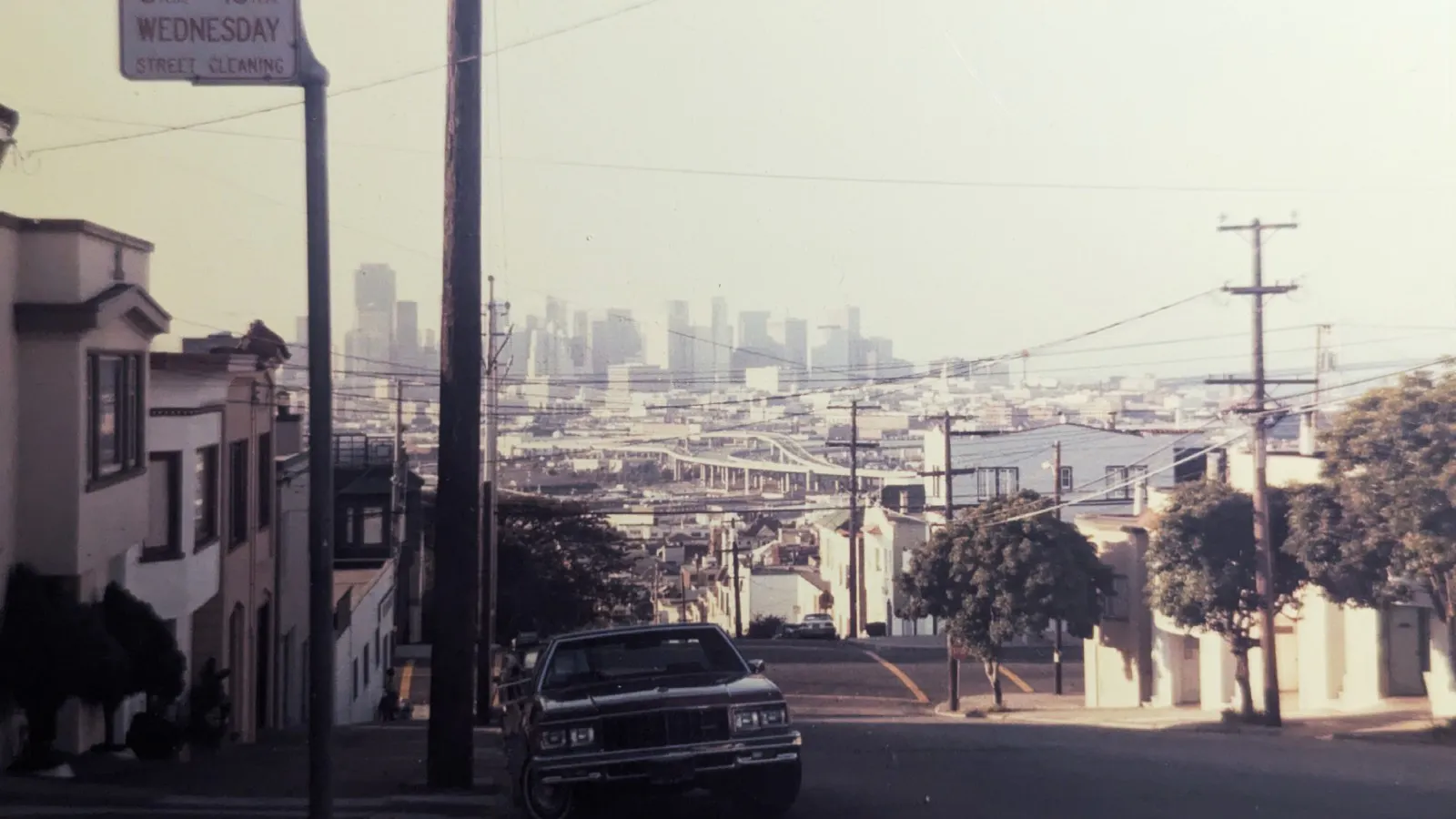 Vergilbtes Foto, Blick auf die sonnenbeschienene Skyline von San Francisco, am Straßenrand ein Straßenkreuzer, im Mittelgrund Freeway-Flyover.