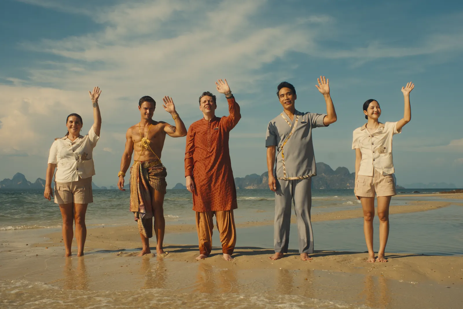 Die Mitarbeiter des Hotels in der 3. Staffel von White Lotus. Sie stehen alle in einer Reihe am Strand und winken den ankommenden Gästen zu.