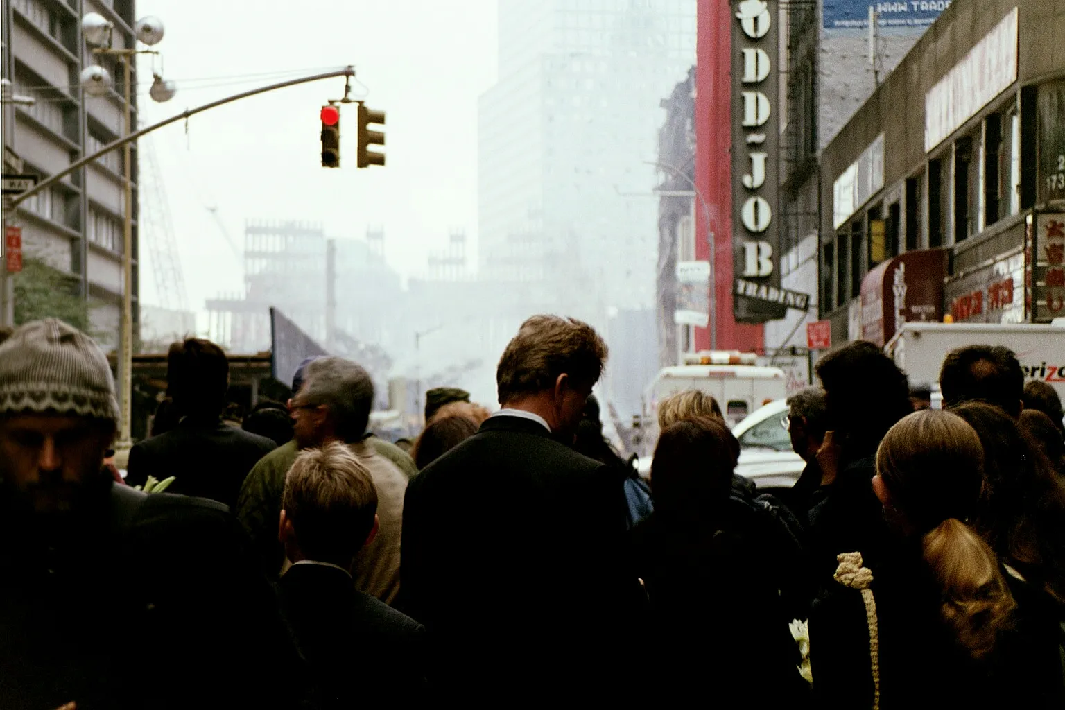Lower Manhattan, ein Blick über eine Menschenmenge hinweg, am Ende einer Straße sieht man Trümmer des World Trade Centers, Rauch hängt in der Luft.