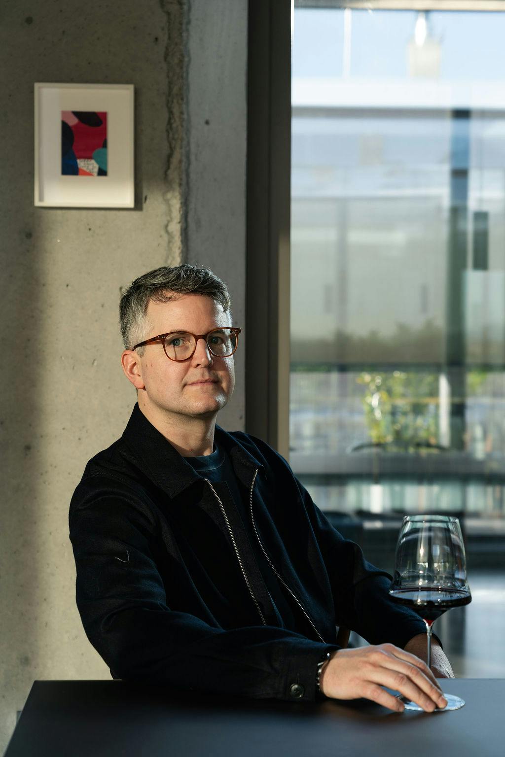 Ein Mann sitzt an einem Tisch. Vor ihm steht ein Weinglas mit Rotwein