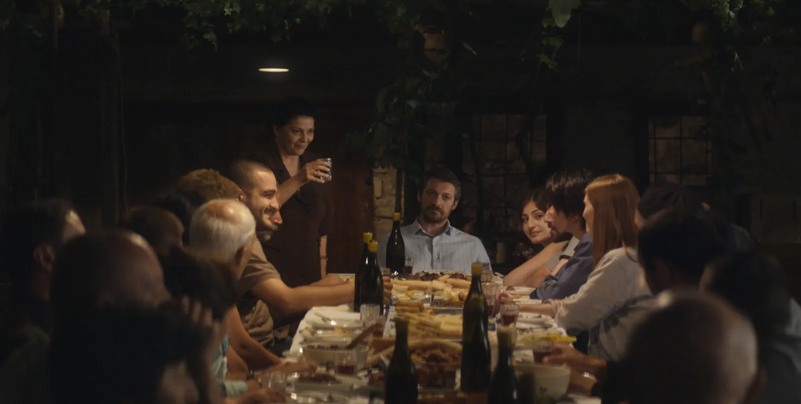Eine Familie sitzt an einem langen Tisch, auf dem Weinflaschen und Essen steht